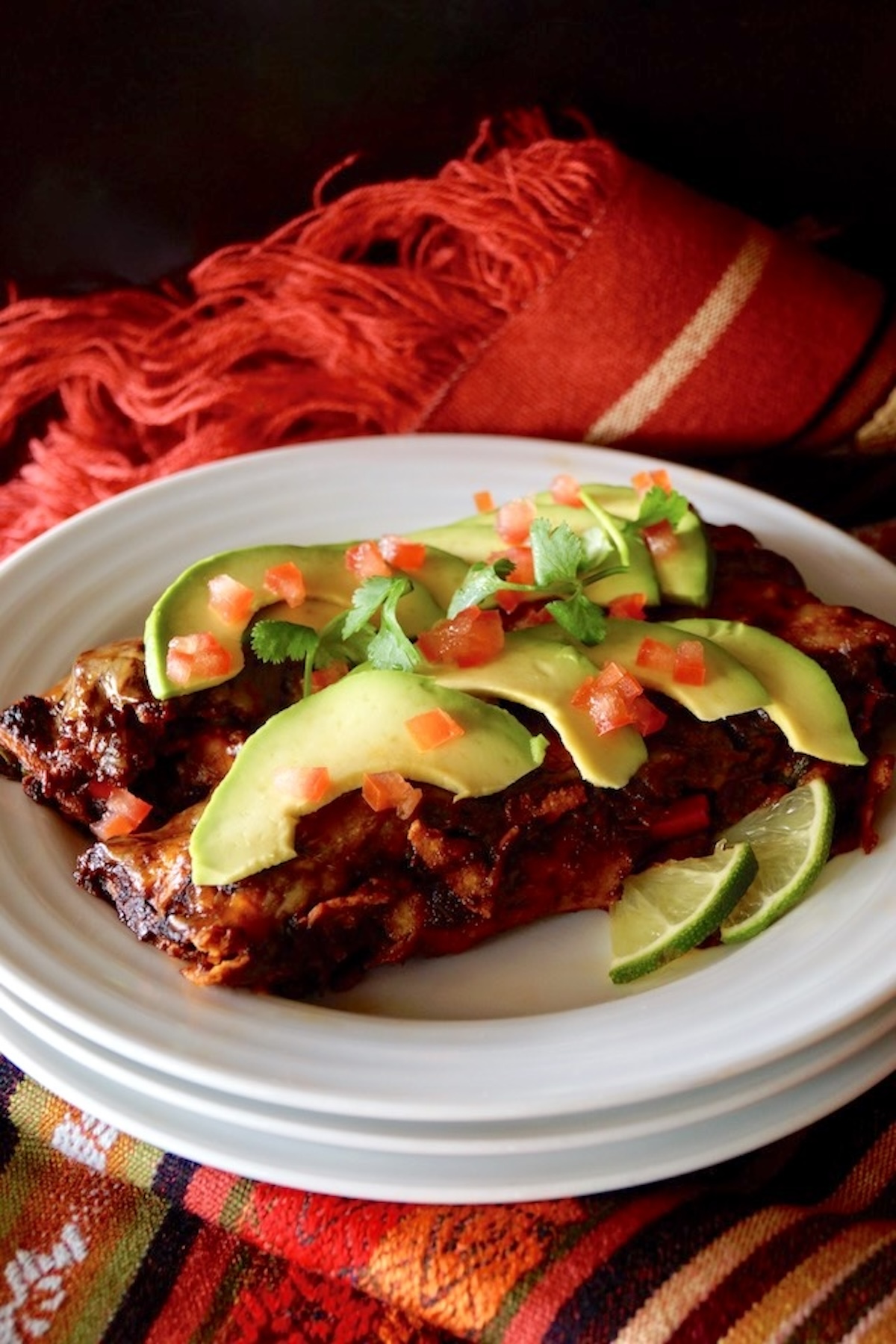Two vegetarian enchiladas on a white plate, with avocado slices and diced tomato on top.