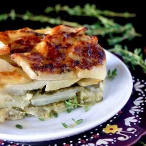 1 serving of Gruyere Spinach Potatoes Au Gratin on a white plate surround by fresh thyme sprigs.