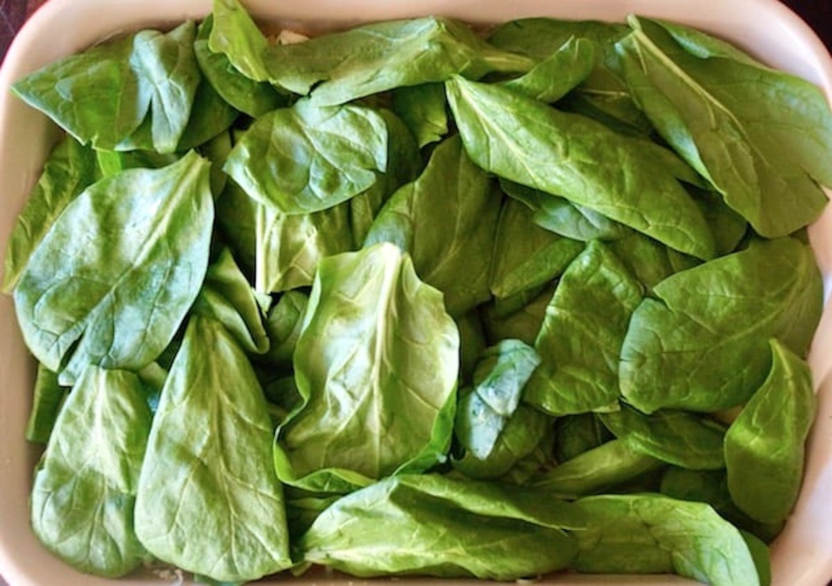 Casserole dish filled with spinach leaves.