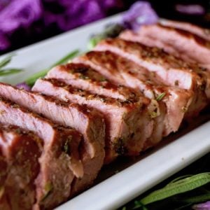 Several slices of pink-ish ribeye steak with lavender on a white plate