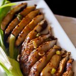 Close up of sliced Marinated Grilled Portabello Mushrooms on a white rectangular plate with green onions.