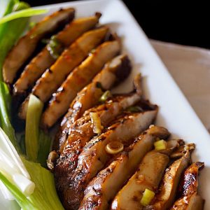 Close up of sliced Marinated Grilled Portabello Mushrooms on a white rectangular plate with green onions.