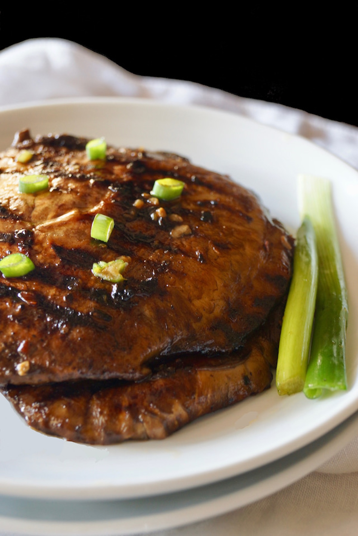 Whole Marinated Grilled Portabello Mushrooms on a white plate with green onions.