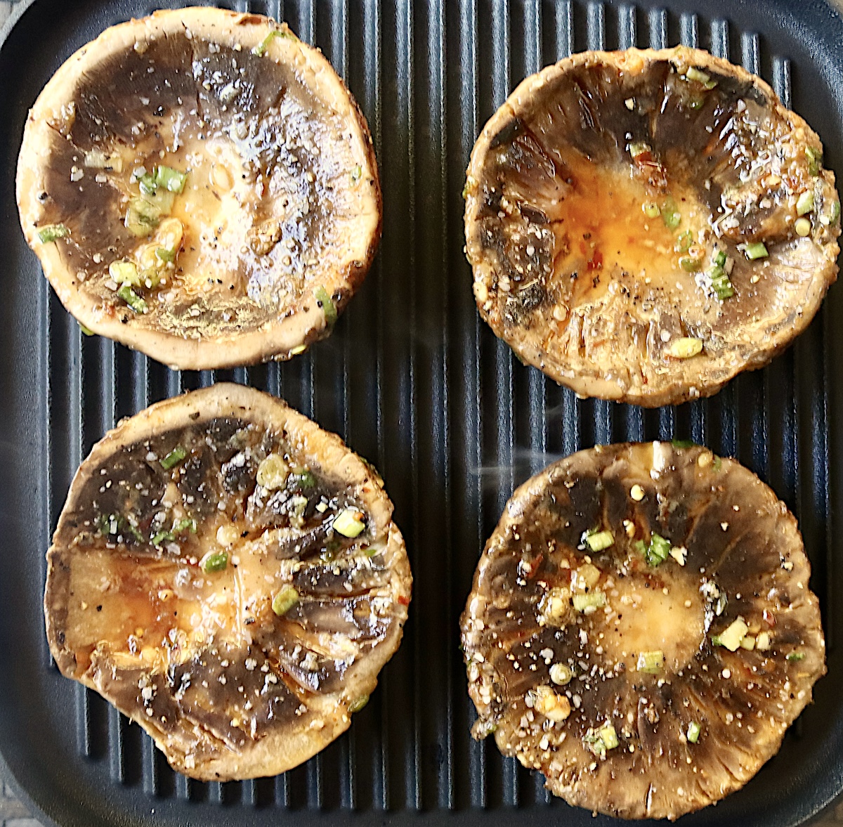 Marinated-Grilled-Portobello-Mushrooms 4 portobello mushrooms, round side down, on a grill.