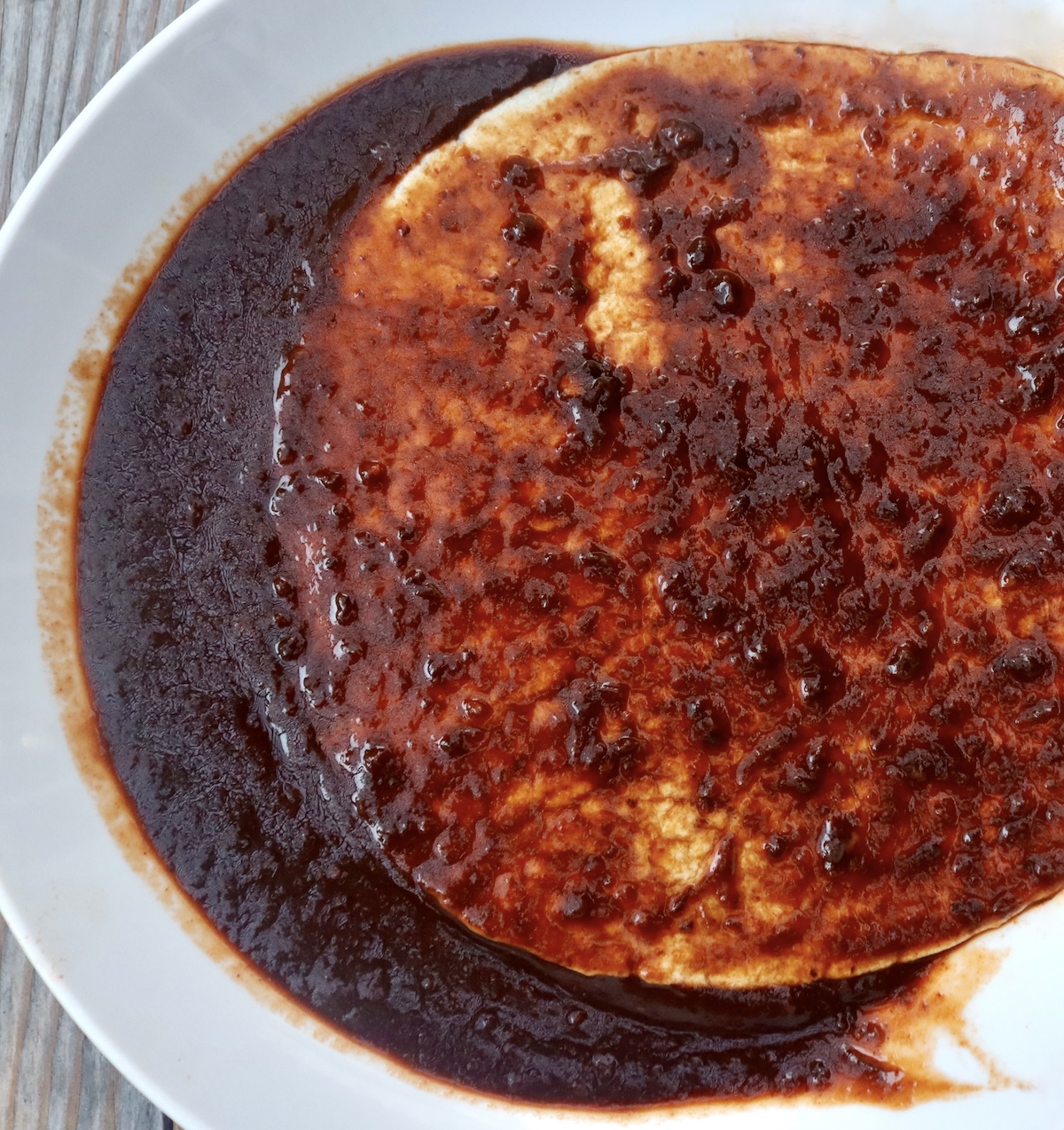 One tortilla being dredged into enchilada sauce in a shallow bowl.