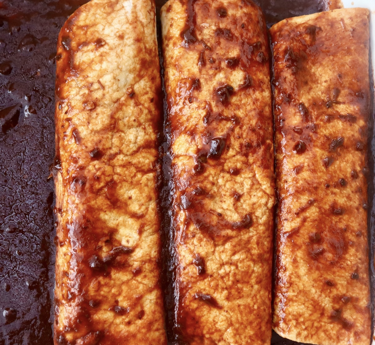 Three rolled and sauced tortillas for enchiladas.