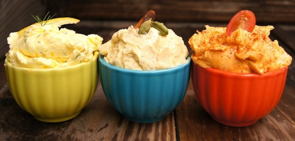 Three different compound butters in small yellow, blue and red bowls. (Meyer Lemon-Dill Butter, Spiced Chai Butter & Smoky Tomato Butter)