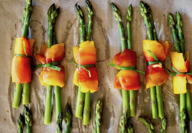 Several bundles of asparagus wrapped in the center with a roasted piece of an Enjoya pepper, and tied with a chive.