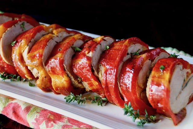 Enjoya-Wrapped Pork Tenderloin with Salami and Provolone, sliced neatly on a white plate with fresh thyme.