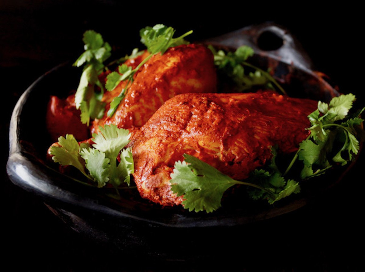 Marinated Achiote Chicken Recipe in black ceramic bowl with fresh cilantro.