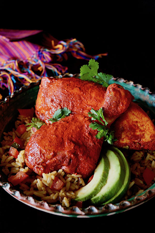 Drumstick and breast of Marinated Achiote Chicken Recipe with avocado slices and cilantro.