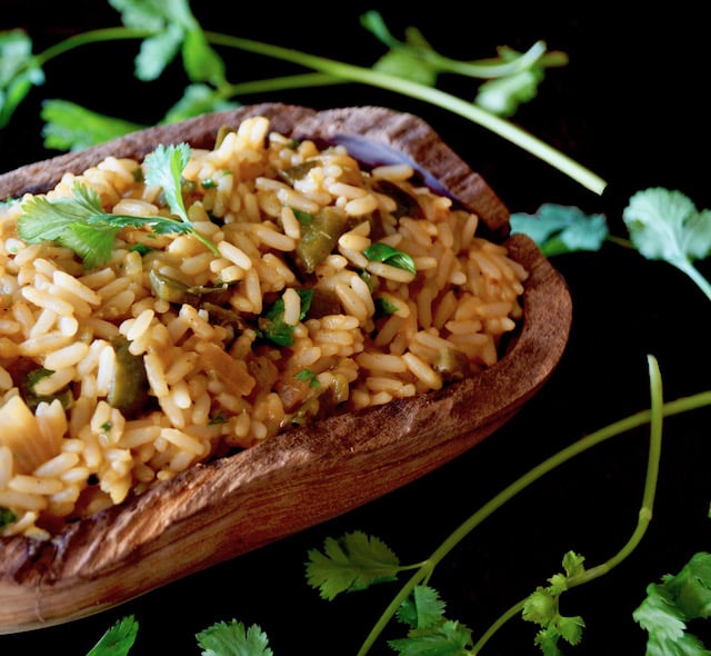 Mexican Poblano Rice Pliaf in a wooden, oval-shpaed bowl with cilantro sprigs on black background.