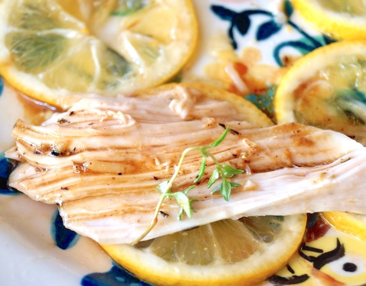 Simple-Lemon-Roasted-Chicken Shredded chunk of roasted chicken with lemon slices and juice from the pan.