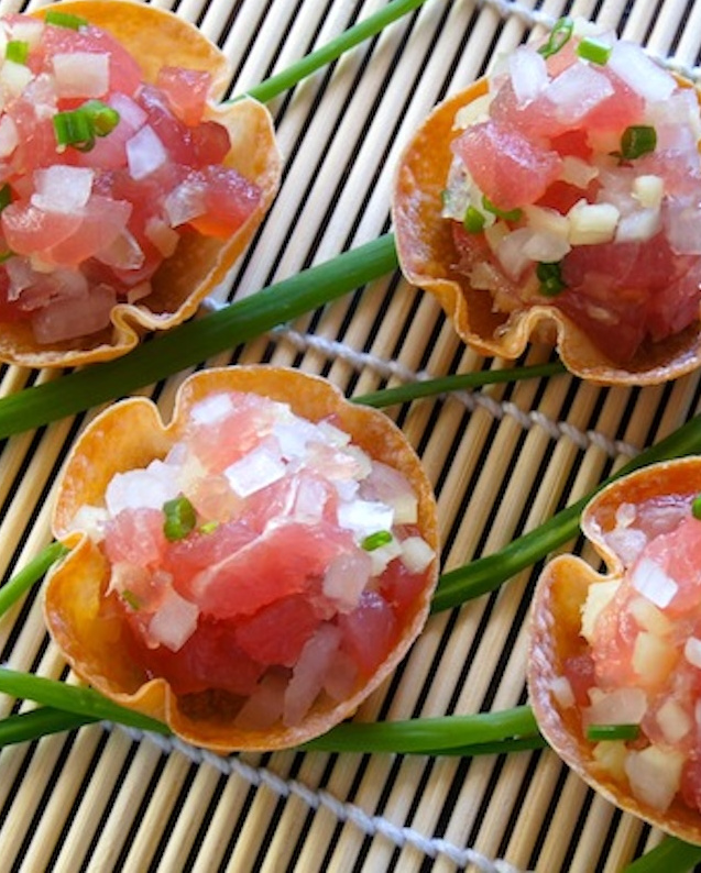 Ahi-Tuna-Tartare-with-Ginger 4 wonton cups with ahi tuna tartare on top of chives on a sushi mat.