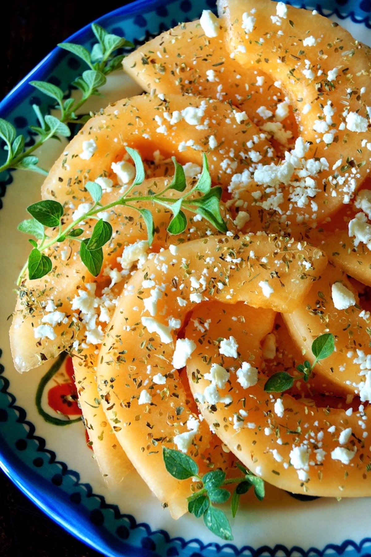 Cantaloupe-Feta-Salad-with-Oregano Close up of sliced orange melon sprinkled with fresh and dried oregano and crumbled Feta.