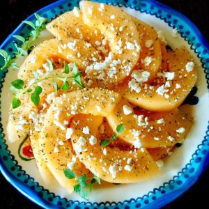 Blue-rimmed plate with sliced orange melon sprinkled with fresh and dried oregano and crumbled Feta.