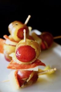 Roasted Hatch Chile wrapped around a red grape with a slice of Chorizo and cheese, all on a toothpick.