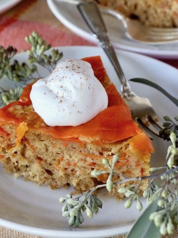 Three small slices of upside down carrot cake on white plates with a dollop of whipped cream on each one.