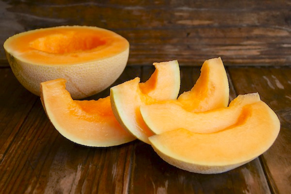 Cantaloupe-Feta-Salad-with-Oregano Bright orange melon cut in half and then into thick slices.on a dark wood background.