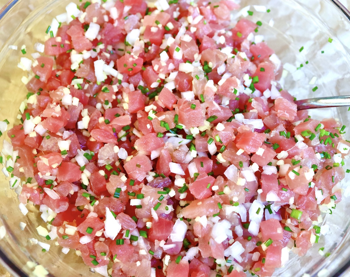Ahi-Tuna-Tartare-with-Ginger Mixed, finely chopped ingredients in a glass bowl for ahi tuna tartare including ahi tuna, white onion, ginger, and chives.