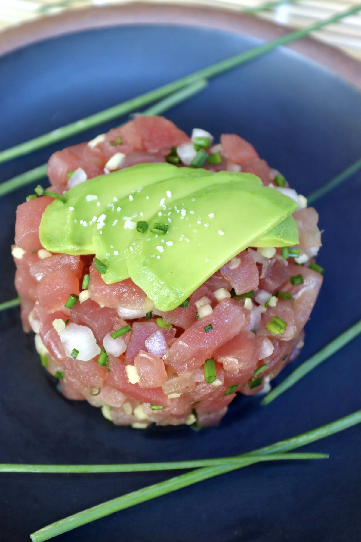 Top view of a round mound of tuna tartare with bits of ginger and onion, and three thin avocado slices on top.
