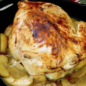 Golden roasted chicken in cast iron skillet with apple slices