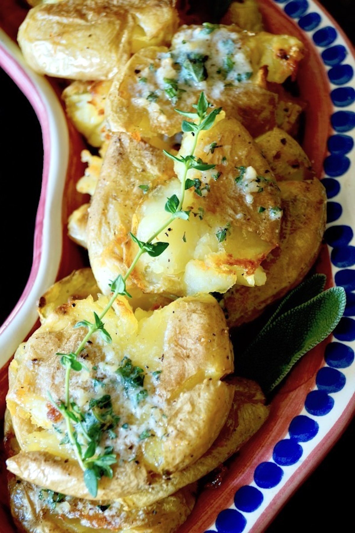 Several garlic smashed potatoes with fresh thyme on a narrow red serving dish.