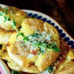 Close up of smashed potatoes with butter and fresh thyme.