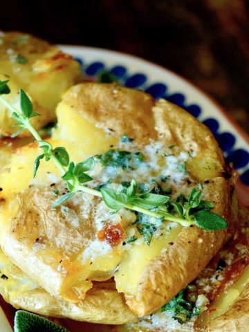 Close up of smashed potatoes with butter and fresh thyme.