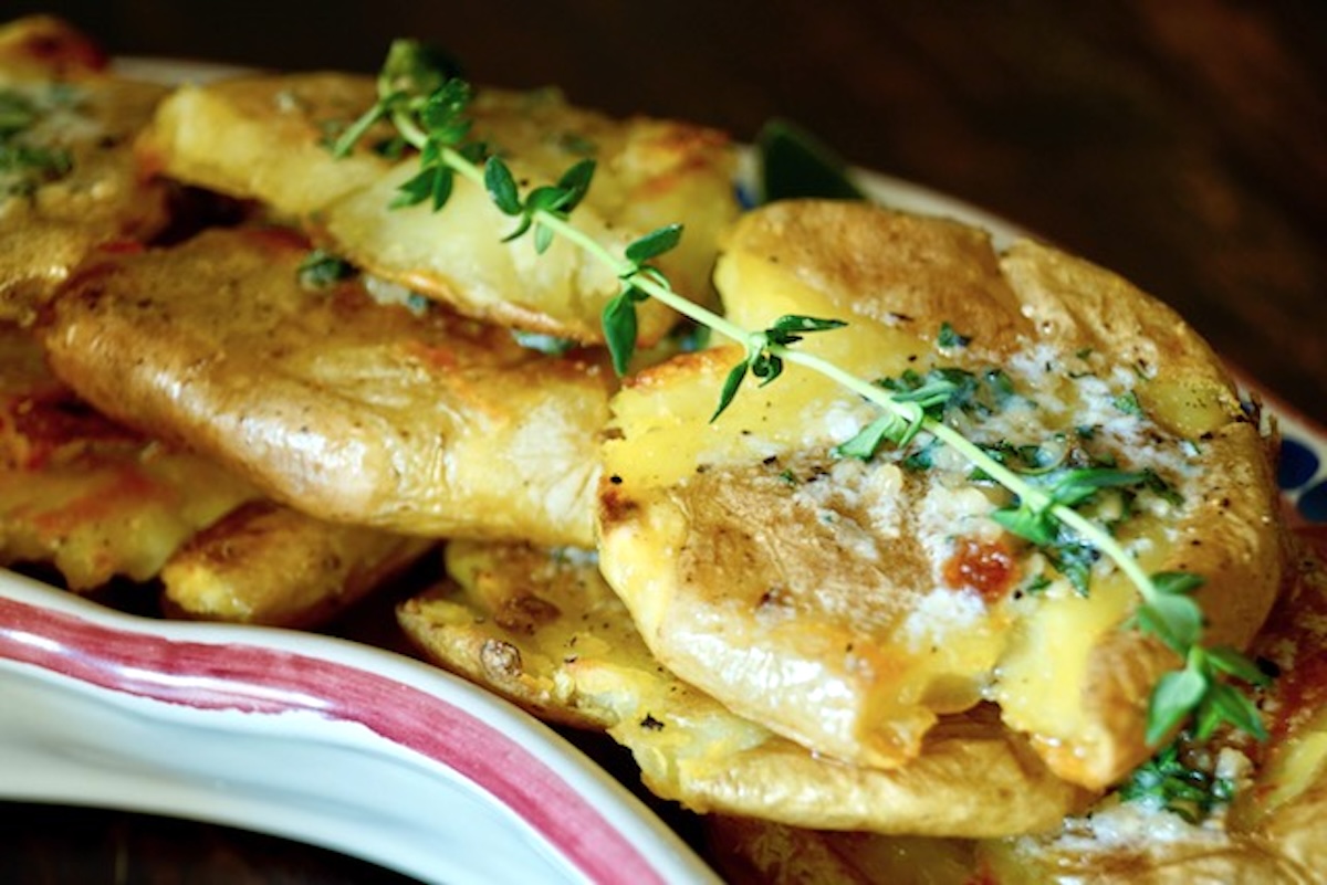 Several garlic smashed potatoes on a narrow plate with a sprig of thyme.