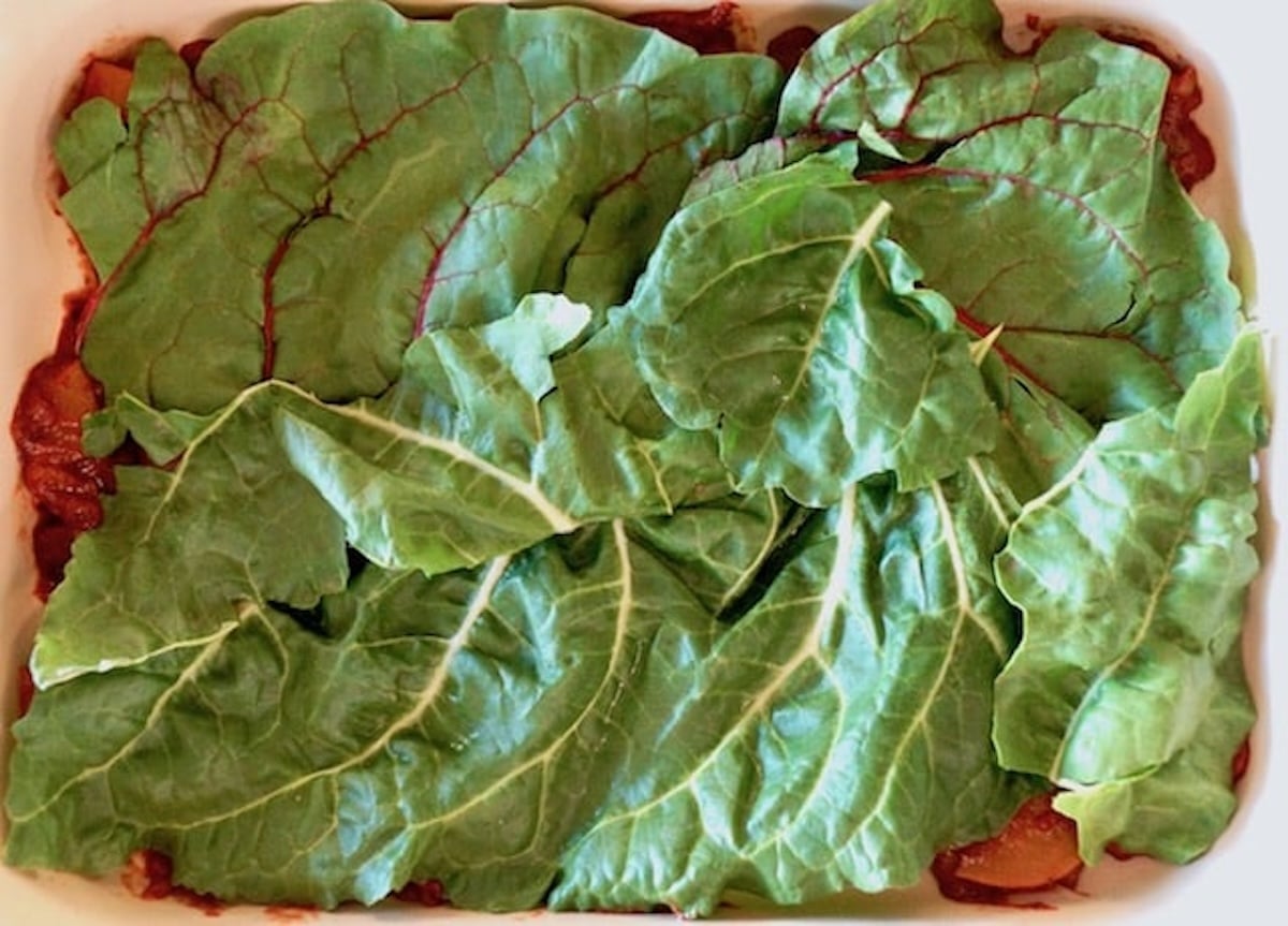 Vegetarian-Swiss-Chard-Lasagna Red sauce with a layer of big chard leaves over it in a casserole dish.