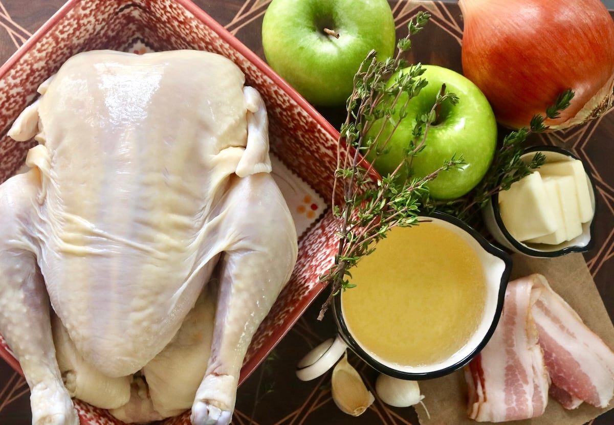 Apple-Roasted Chicken Ingredients for Apple Roasted Chicken including raw whole chicken, apples, cider, thyme and onion.