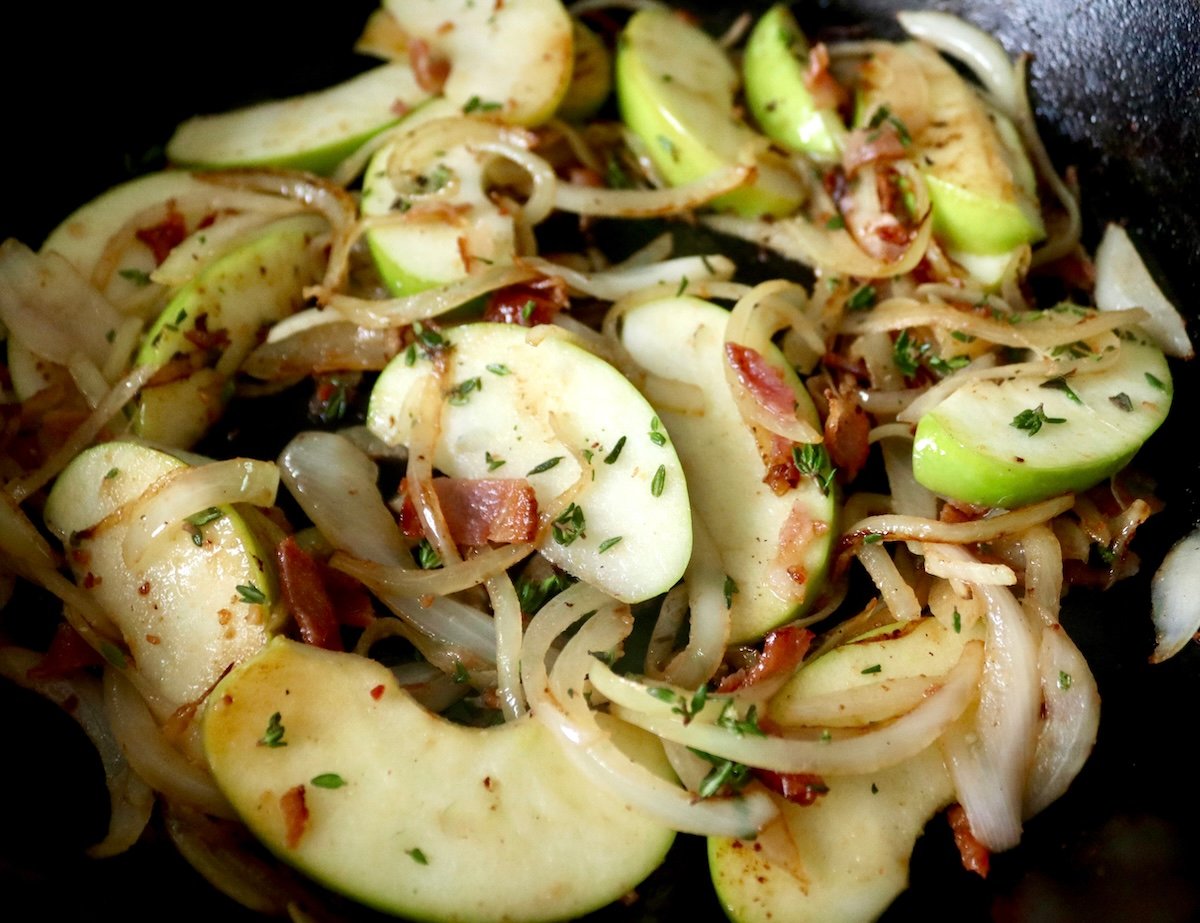 Apple-Roasted Chicken Sliced apples and onions with crumbled bacon and fresh thyme in a cast iron skillet.