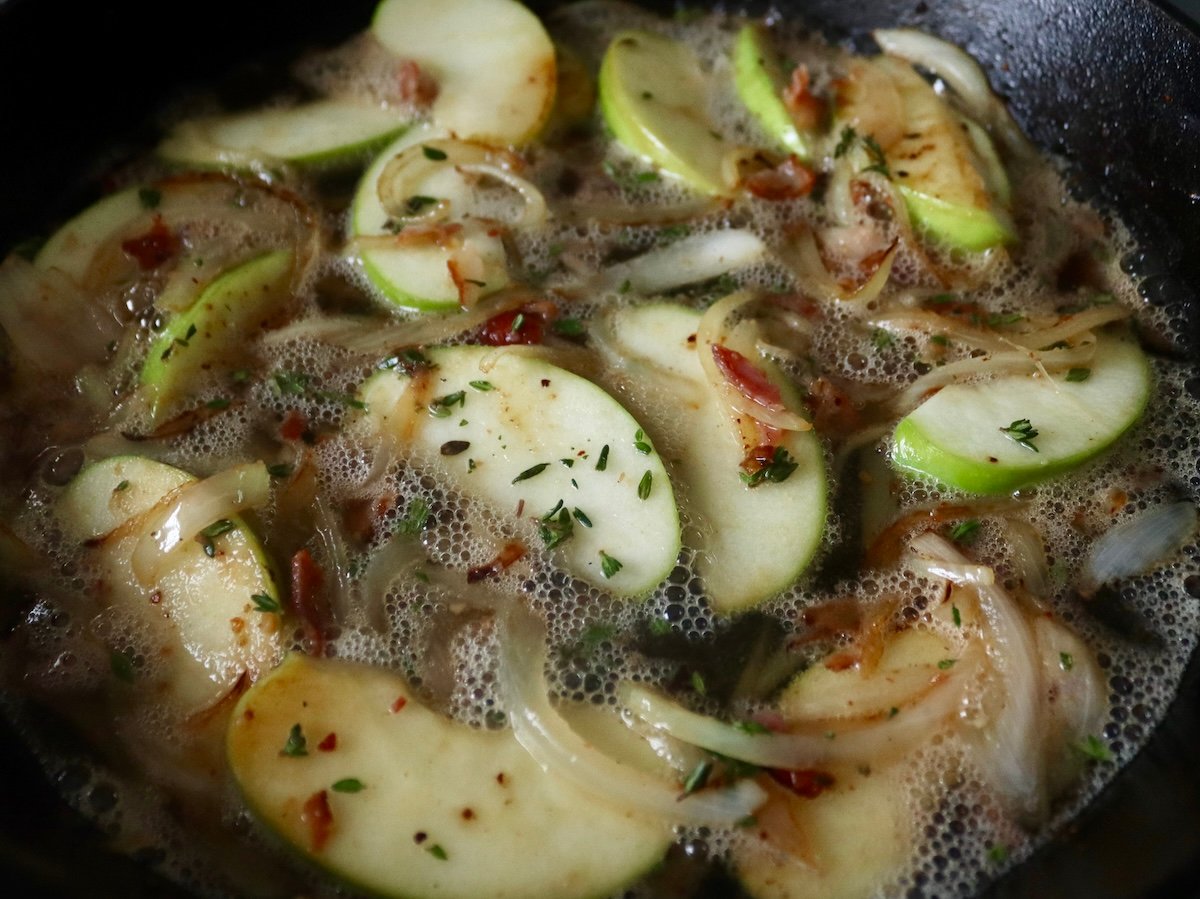 Apple-Roasted Chicken Sliced apples and onions with crumbled bacon, fresh thyme and apple cider, in a cast iron skillet.