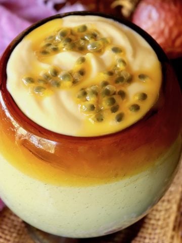 Large glass goblet with caramel-colored rim, filled with passion fruit mousse, with a purple cloth behind it.