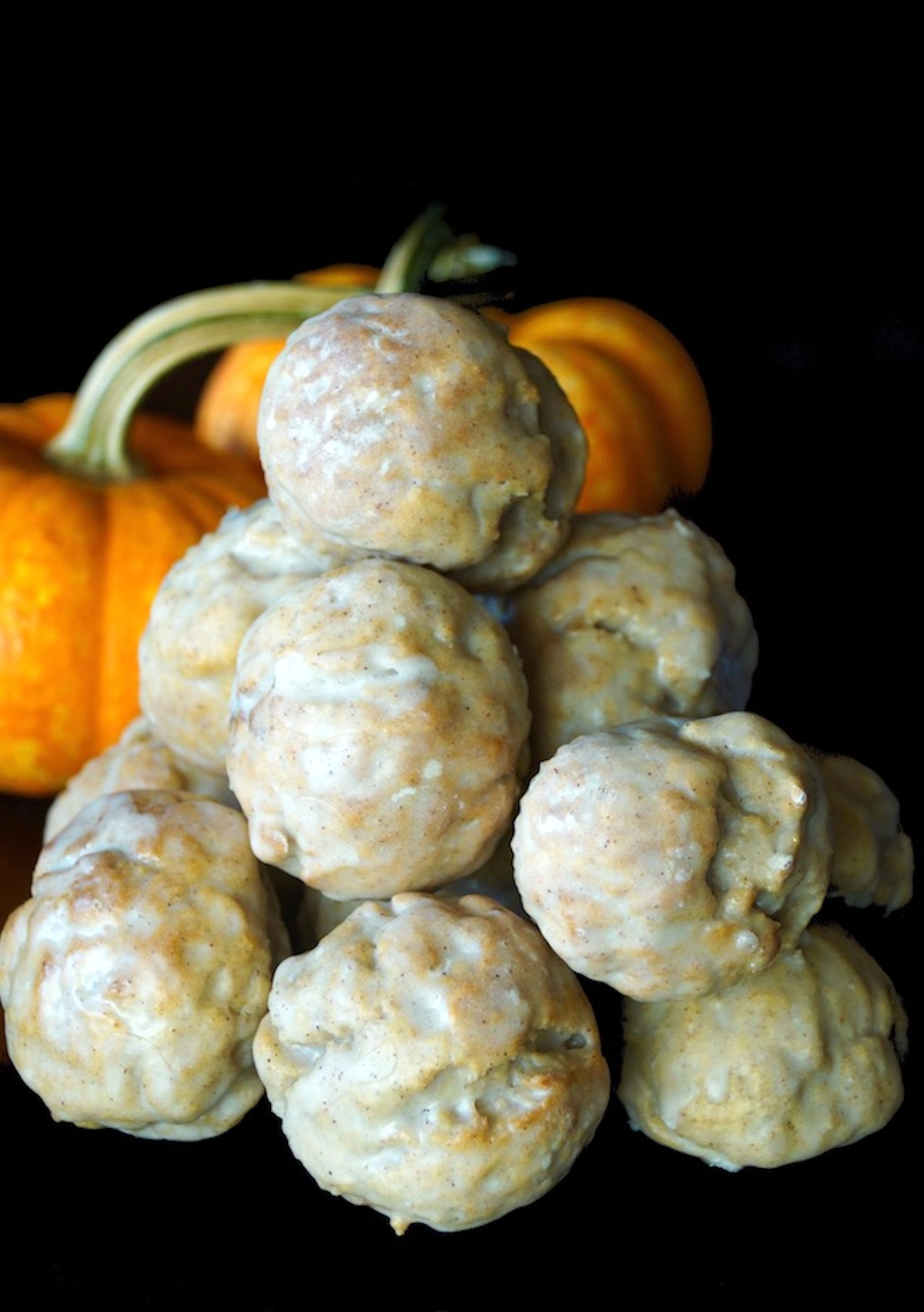 Pumpkin-Air-Fryer-Donut-Holes Tall stack of pumpkin donut holes with black background and a pumpkin behind it.