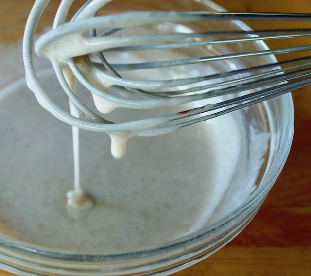 Close up of glaze on a whisk for Air Fried Pumpkin Spice Glazed Donut Holes.