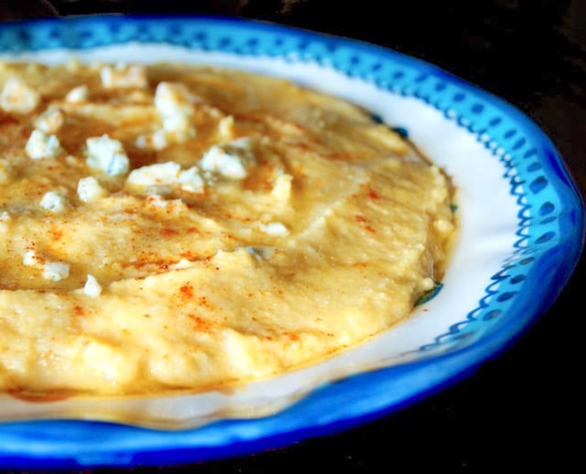 Bright blue-rimmed bowl with creamy polenta with gorgonzola sprinkled on top.