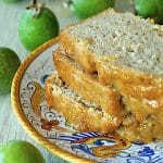 Three slices of Glazed Pineapple Guava Bread on an Italian ceramic, gold-rimmed plate, surrounded by fresh green guavas.