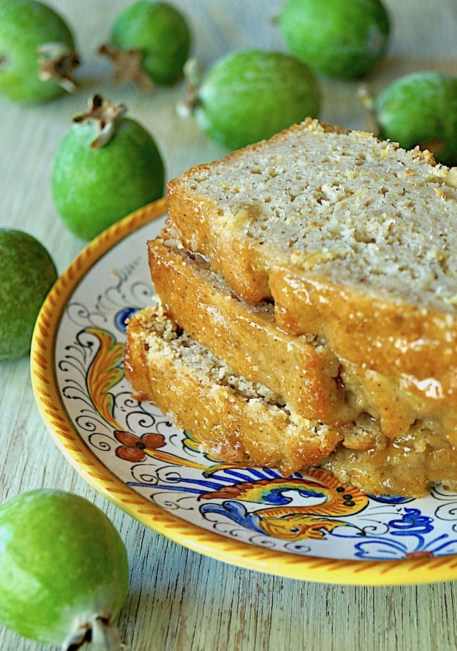 Three slices of Glazed Pineapple Guava Bread on an Italian ceramic, gold-rimmed plate, surrounded by fresh green guavas.