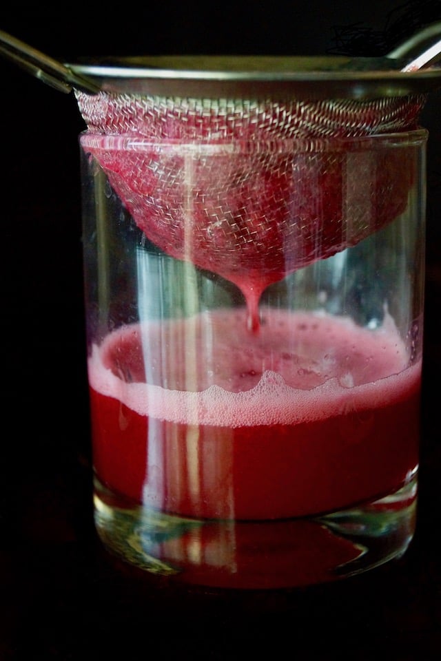 Small strainer over a glass with pomegranate juice