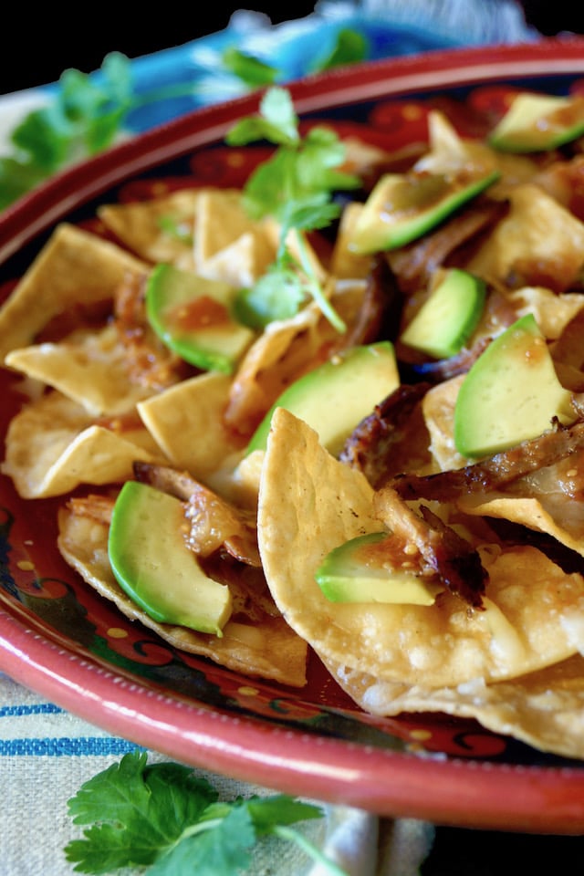 Close up of red plate full with Spiced Pulled Pork Nachos with avocado slices.