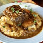 White bowl filled with polenta, topped with braised beef short ribs in pumpkin sauce.