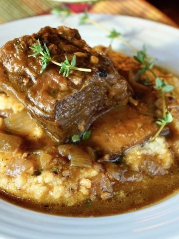 White bowl filled with polenta, topped with braised beef short ribs in pumpkin sauce.