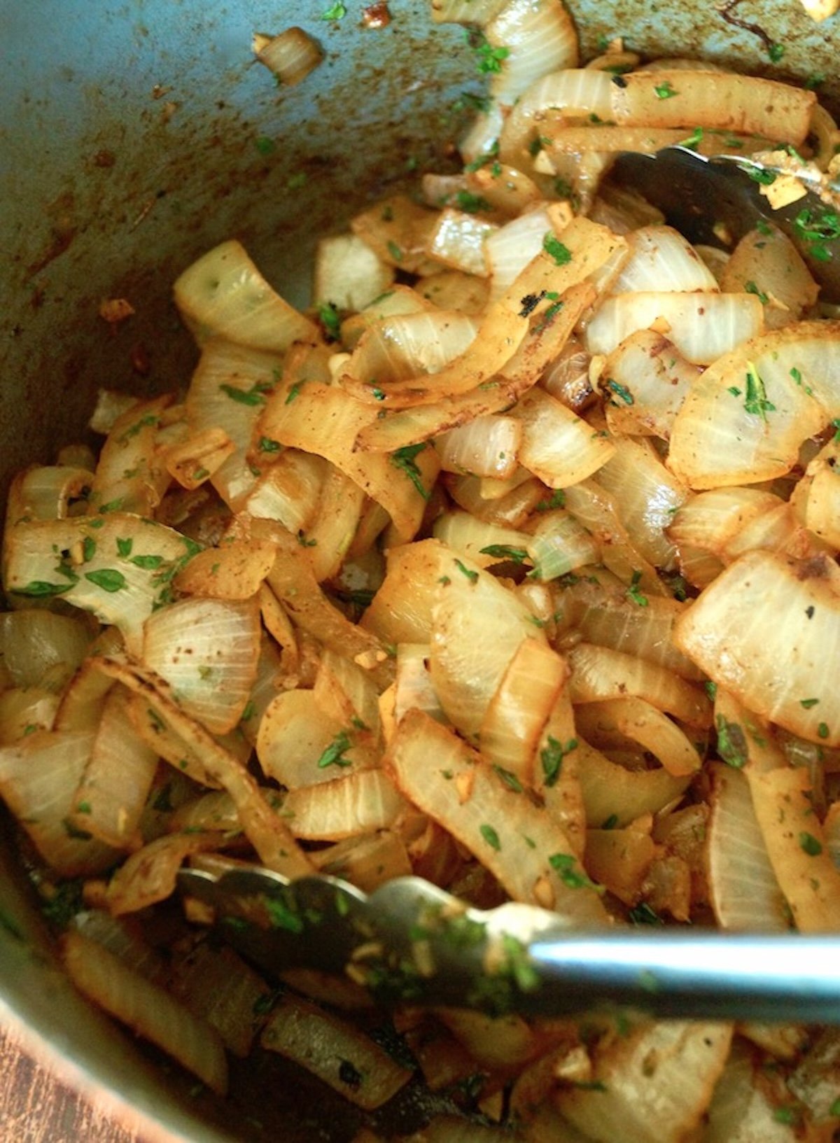 Golden brown onion and fresh thyme in a large Dutch oven with metal cooking tongs.