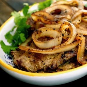 Steak with lots of golden onions on top with greens on the side.