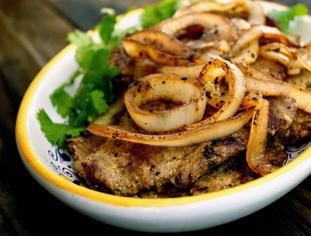 Bistec Encebollado with extra golden onions on top with greens on the side.