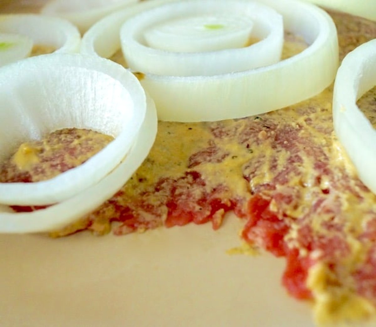 Raw thinly pounded steak with a spread of mustard and raw onoins on top.