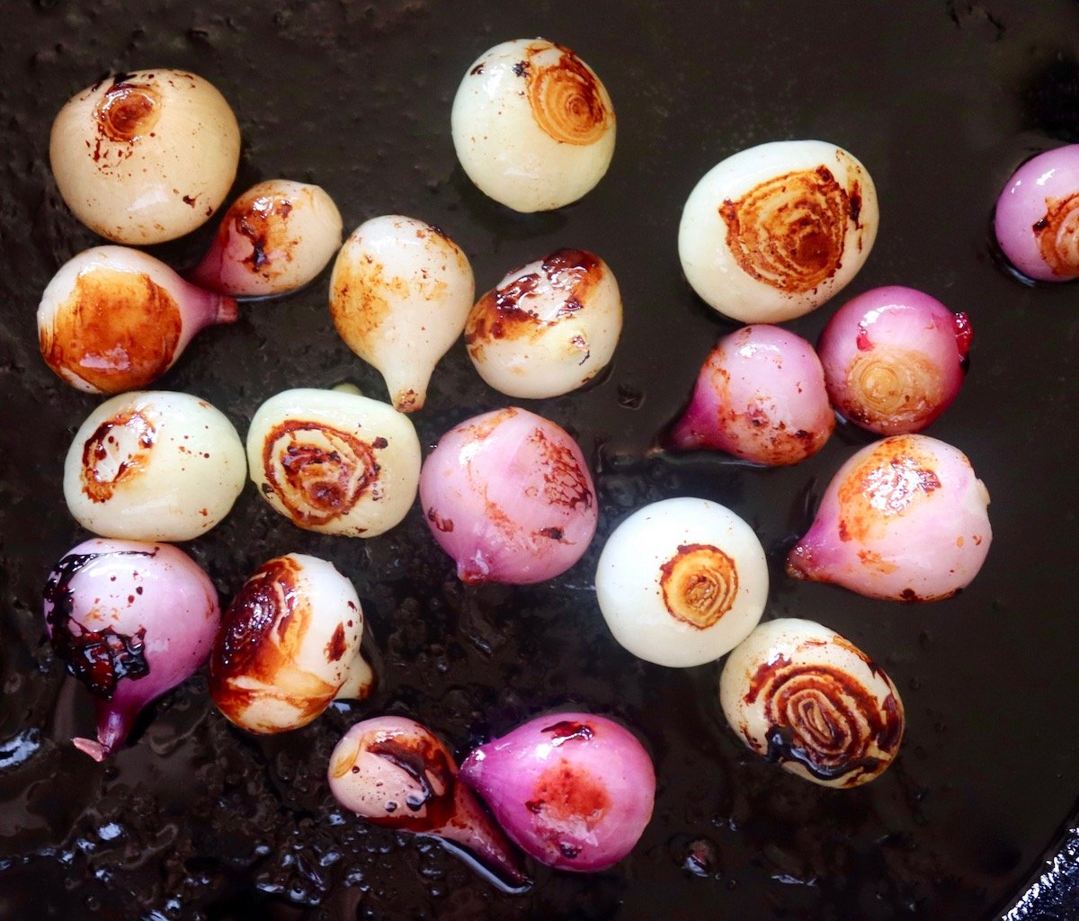 Caramelized purple and white pearl onions in a cast iron skillet.
