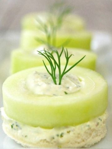 4 Cucumber Canapes lined up vertically on white narrow plate with fresh dill poking up from each one.